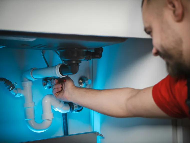 Plumber repairing pipework underneath a kitchen sink