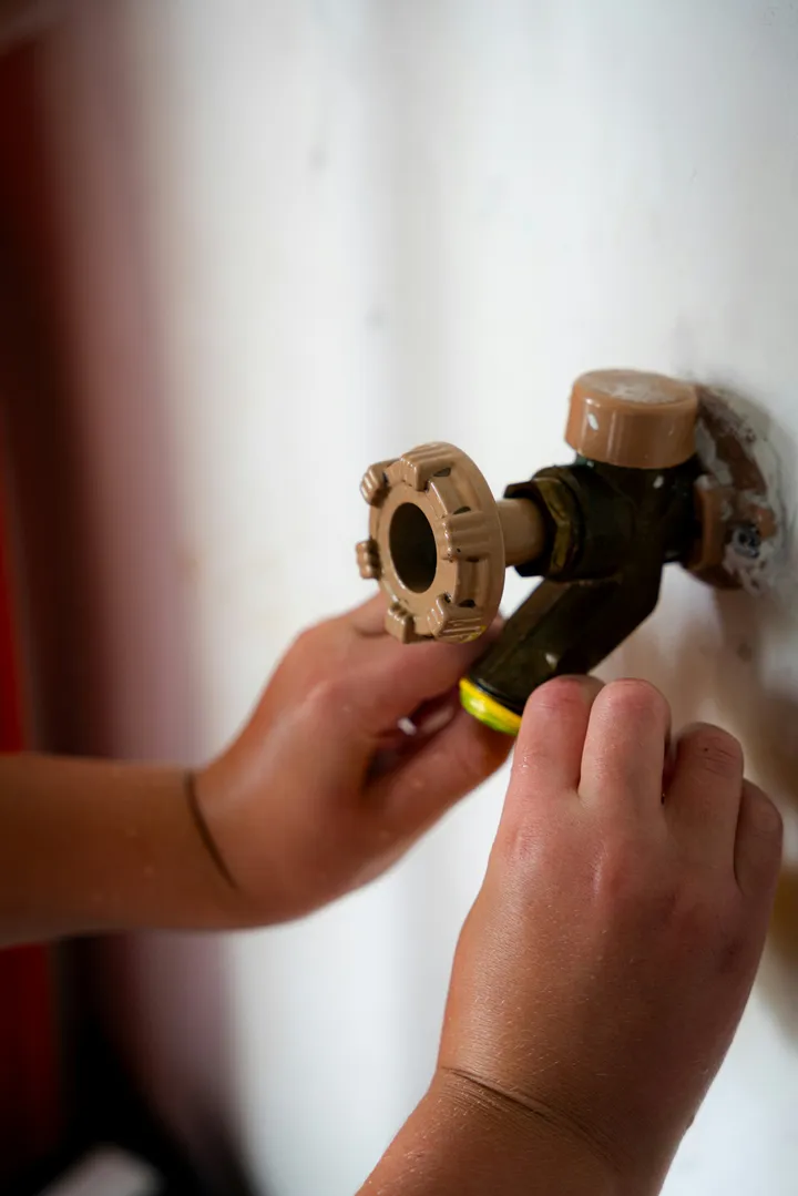 Hands fitting a hose connector to a brass outdoor wall tap