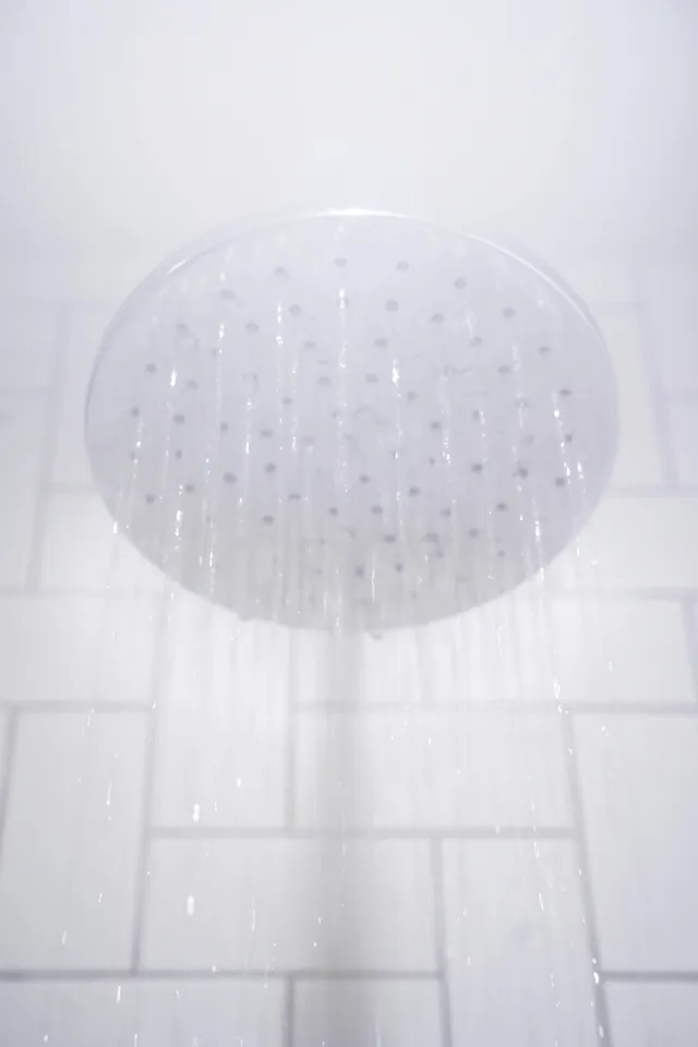 Water falling from a round chrome rainfall shower head against white tiles