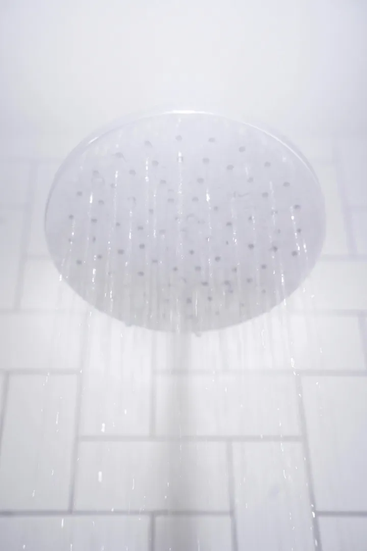 Water falling from a round chrome rainfall shower head against white tiles
