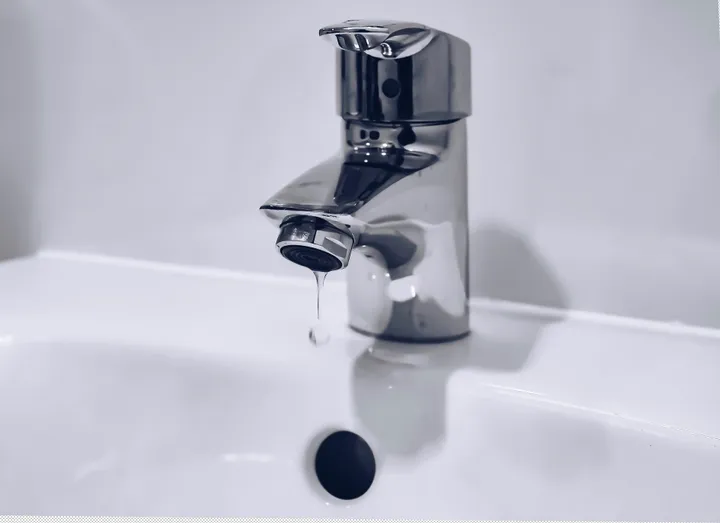 Chrome single-lever basin mixer tap on a white basin with a drip forming